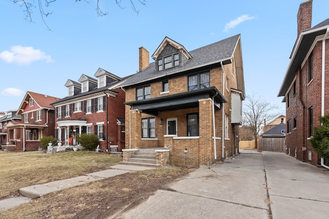 american foursquare style home with covered porch, brick siding, a chimney, and a front lawn