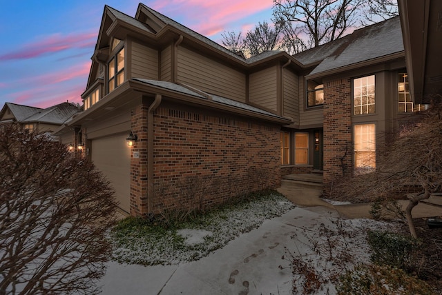 property exterior at dusk featuring a garage and brick siding