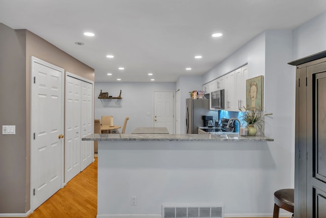 kitchen with visible vents, light stone countertops, stainless steel appliances, light wood-style floors, and white cabinetry