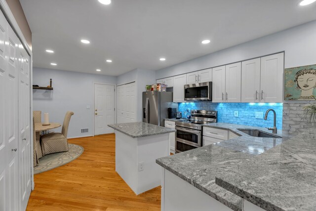 kitchen featuring a center island, light wood finished floors, appliances with stainless steel finishes, white cabinetry, and a sink