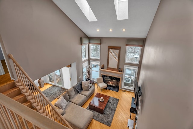 living room featuring high vaulted ceiling, a skylight, wood finished floors, a high end fireplace, and stairs