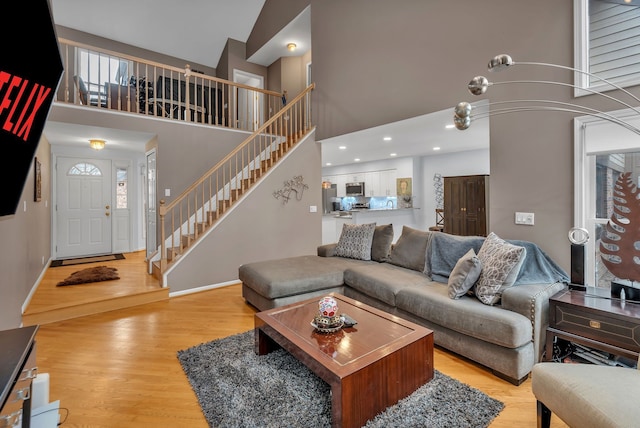 living room featuring stairs, a towering ceiling, and light wood-style floors