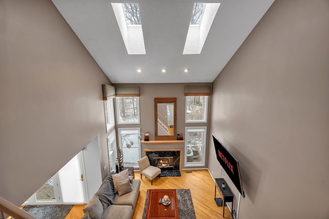 living area featuring a skylight, wood finished floors, a fireplace, high vaulted ceiling, and recessed lighting