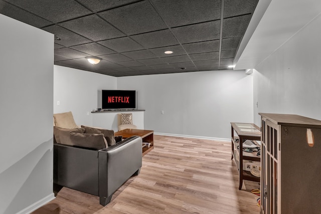 living room featuring a paneled ceiling, baseboards, and wood finished floors