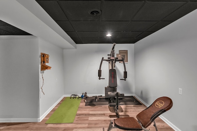 workout room with a paneled ceiling, visible vents, baseboards, and wood finished floors