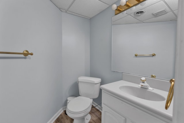 half bathroom with baseboards, a drop ceiling, toilet, wood finished floors, and vanity