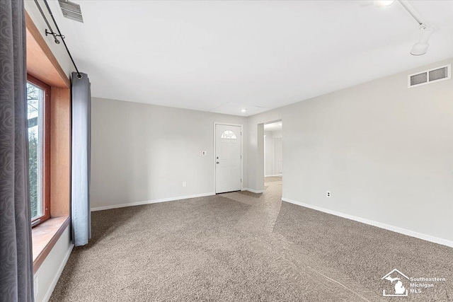 carpeted empty room with baseboards, visible vents, and track lighting