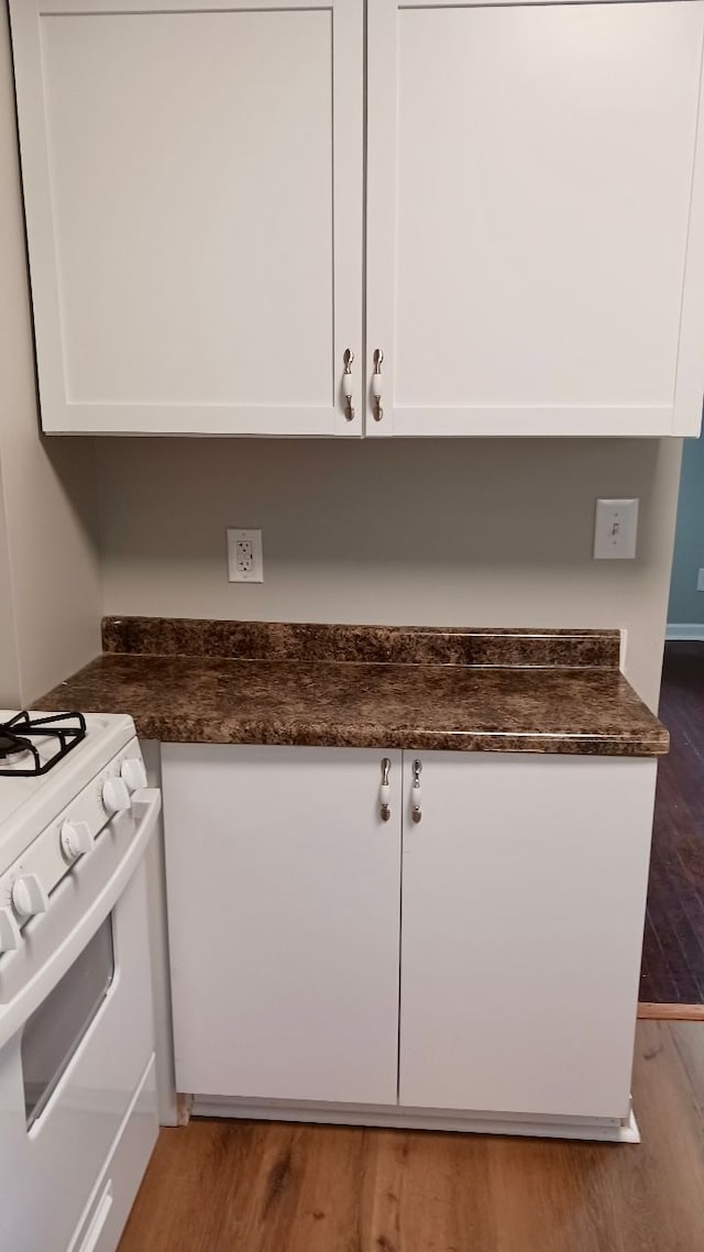 kitchen featuring white range with gas cooktop, dark stone countertops, white cabinetry, and wood finished floors