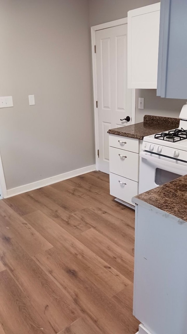 kitchen featuring light wood-style flooring, baseboards, white gas stove, and white cabinetry