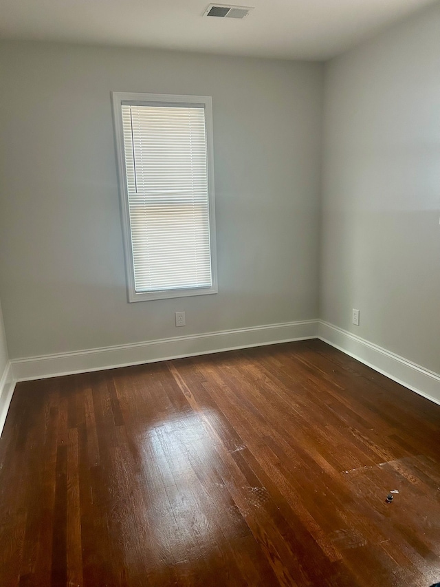 spare room with dark wood finished floors, visible vents, and baseboards