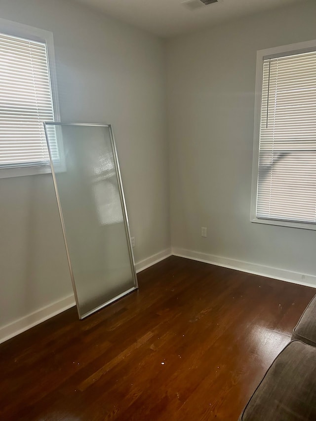 empty room featuring dark wood finished floors, visible vents, and baseboards