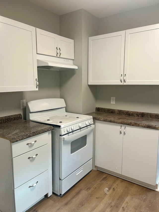 kitchen featuring wood finished floors, white cabinets, white gas range oven, under cabinet range hood, and dark countertops