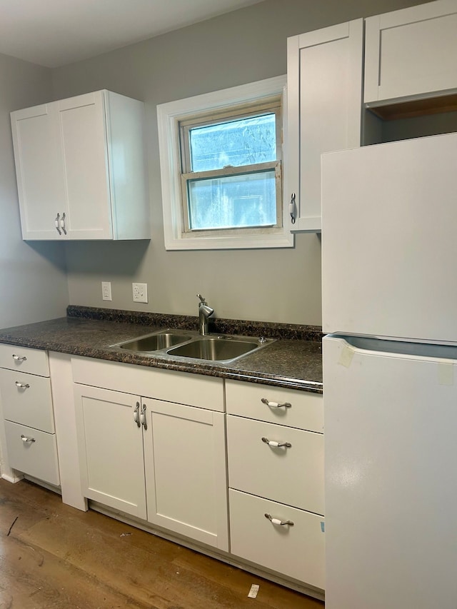 kitchen featuring a sink, light wood finished floors, white cabinets, and freestanding refrigerator