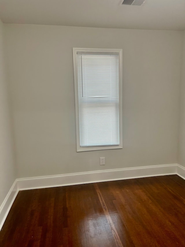 empty room with visible vents, dark wood-type flooring, and baseboards