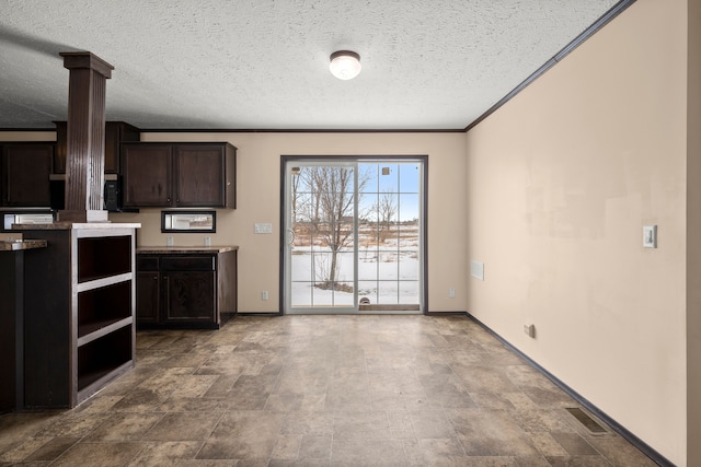 kitchen featuring crown molding, visible vents, dark brown cabinetry, a textured ceiling, and baseboards