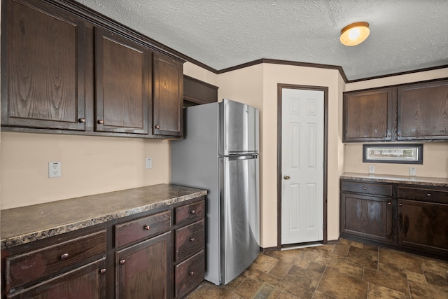 kitchen with ornamental molding, freestanding refrigerator, dark brown cabinetry, and dark countertops