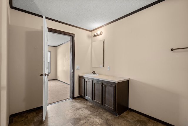 bathroom with a textured ceiling, vanity, baseboards, ornamental molding, and stone finish flooring