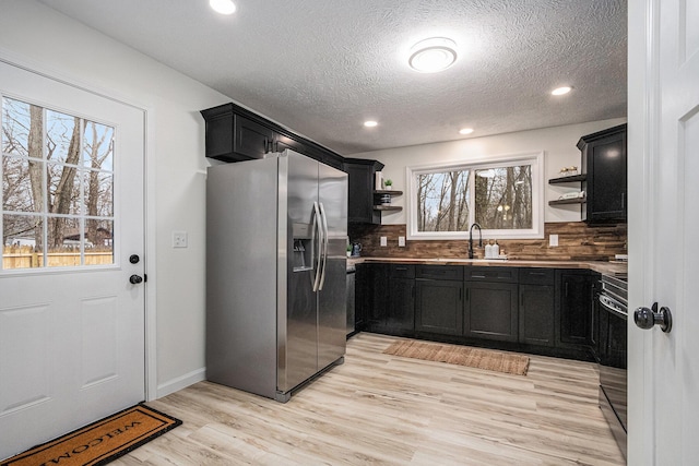 kitchen featuring open shelves, appliances with stainless steel finishes, dark cabinetry, and a sink