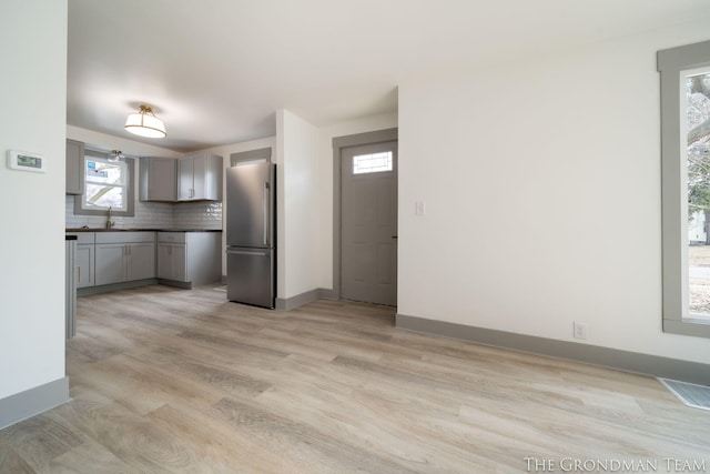 kitchen with gray cabinetry, visible vents, light wood-style floors, freestanding refrigerator, and tasteful backsplash