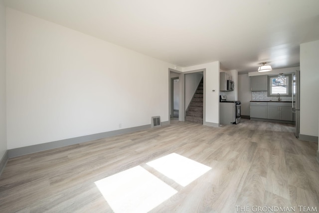 unfurnished living room featuring visible vents, light wood-style flooring, a sink, baseboards, and stairs