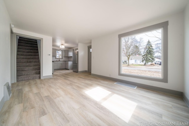 unfurnished living room featuring baseboards, visible vents, light wood finished floors, and stairs