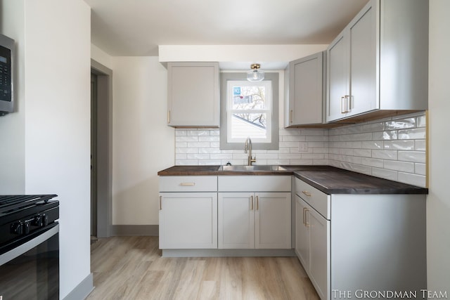 kitchen featuring butcher block counters, a sink, black range with gas stovetop, light wood finished floors, and tasteful backsplash