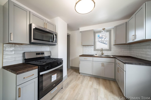 kitchen with light wood-style flooring, appliances with stainless steel finishes, gray cabinetry, wooden counters, and a sink