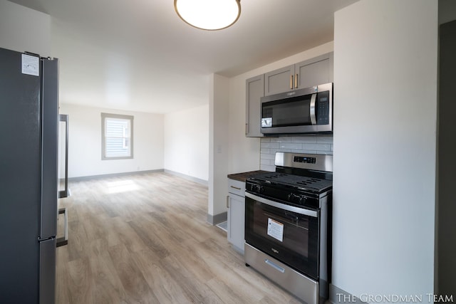 kitchen featuring gray cabinetry, stainless steel appliances, baseboards, light wood-type flooring, and tasteful backsplash