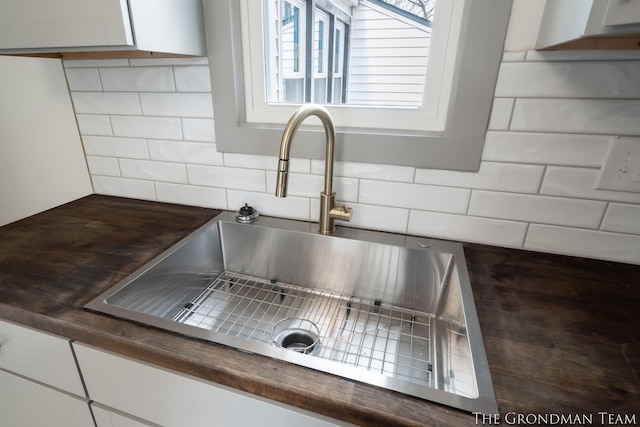 details with tasteful backsplash, dark countertops, a sink, and white cabinetry