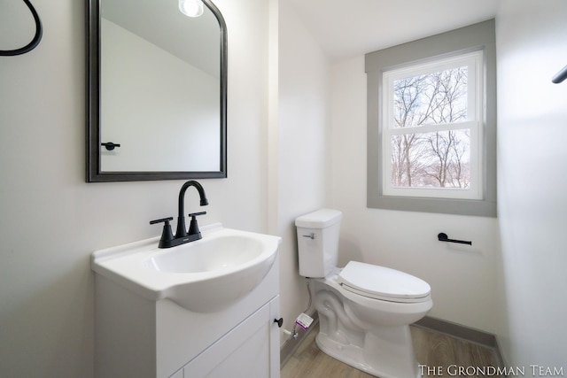 half bath with toilet, wood finished floors, and vanity