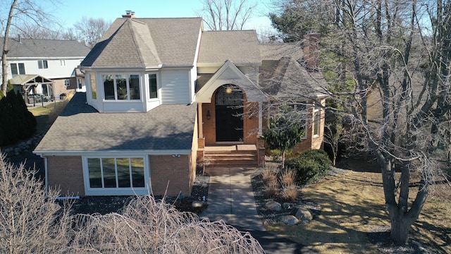 view of front of property with brick siding, roof with shingles, and a chimney