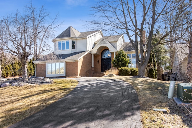 view of front of home featuring aphalt driveway, brick siding, a front lawn, and a shingled roof