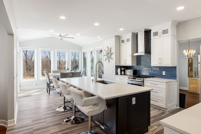 kitchen featuring a sink, decorative backsplash, vaulted ceiling, stainless steel range with electric stovetop, and wall chimney range hood