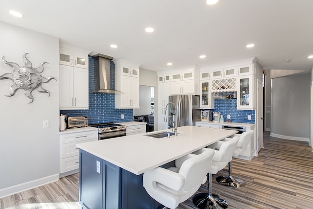 kitchen featuring a breakfast bar area, an island with sink, a sink, stainless steel appliances, and wall chimney exhaust hood