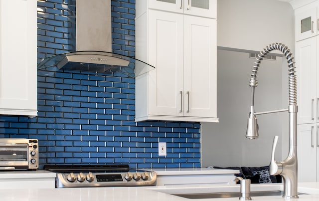 kitchen featuring a toaster, backsplash, white cabinetry, and wall chimney exhaust hood