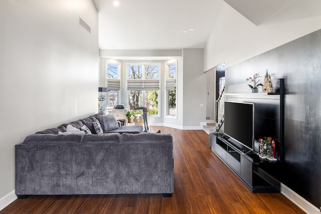 living room featuring dark wood finished floors, baseboards, visible vents, and a towering ceiling