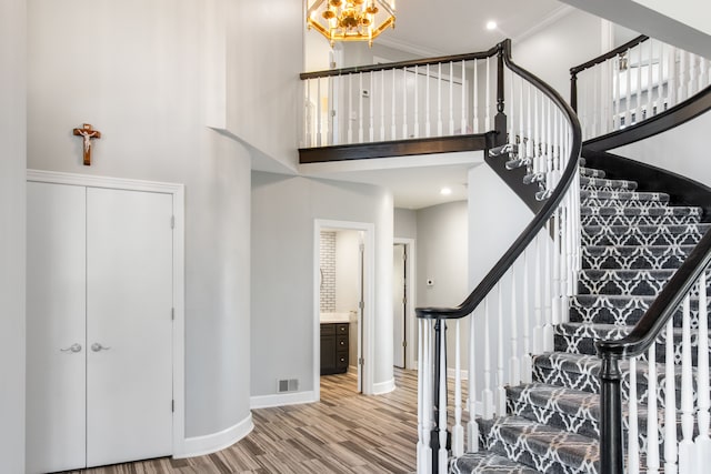 staircase with visible vents, ornamental molding, wood finished floors, baseboards, and a towering ceiling