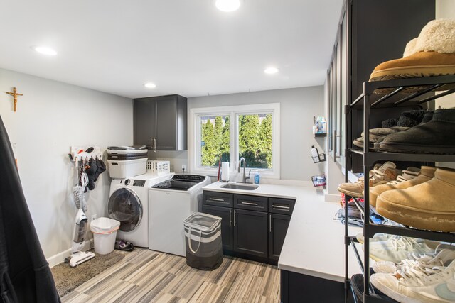 laundry room featuring washing machine and dryer, recessed lighting, light wood-style floors, cabinet space, and a sink