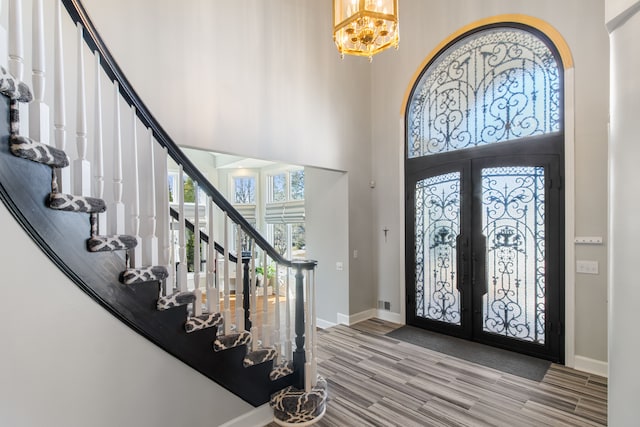 foyer entrance featuring stairway, wood finished floors, baseboards, french doors, and a towering ceiling