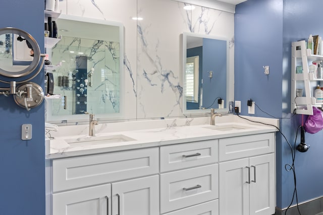 bathroom with a sink, a marble finish shower, and double vanity