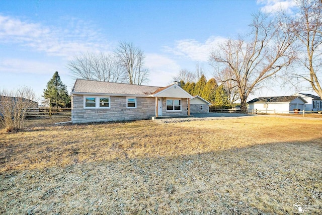 single story home featuring stone siding, fence, and a front yard