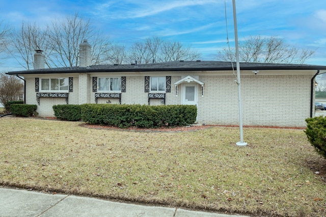 single story home featuring brick siding, a chimney, and a front yard