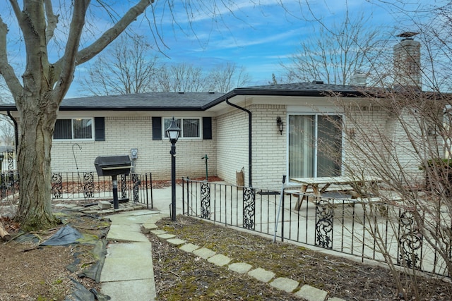 back of property featuring a patio, brick siding, a chimney, and fence