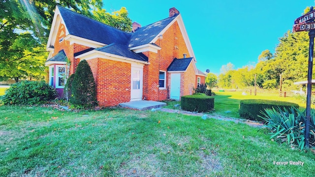 exterior space with brick siding, a yard, a chimney, and roof with shingles