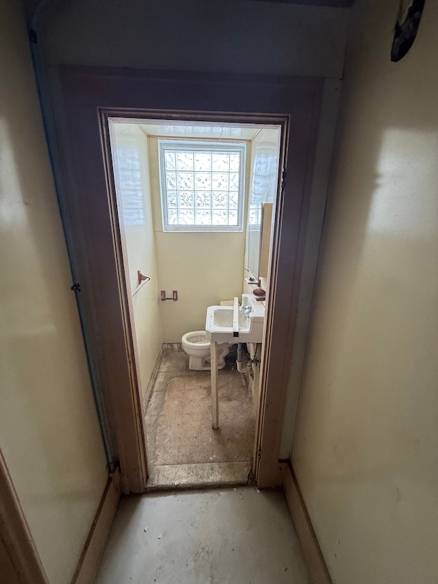 bathroom featuring unfinished concrete floors, toilet, and a sink