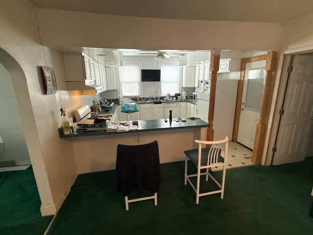 kitchen featuring dark countertops, white appliances, arched walkways, a peninsula, and ceiling fan