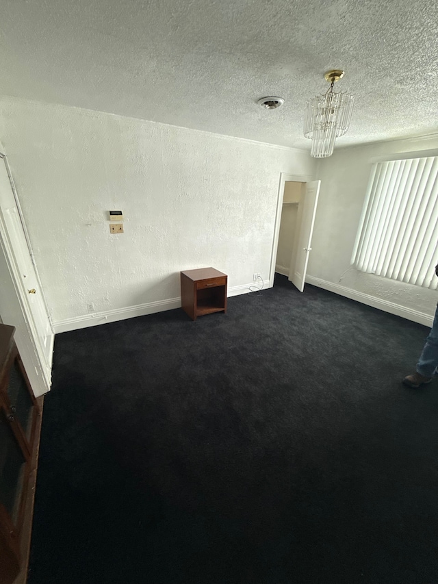 spare room featuring visible vents, a textured ceiling, dark carpet, and a textured wall