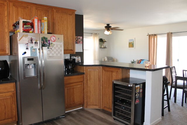 kitchen with beverage cooler, brown cabinets, a peninsula, dark countertops, and stainless steel fridge