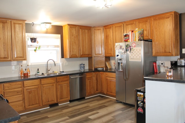 kitchen featuring light wood-type flooring, a sink, appliances with stainless steel finishes, dark countertops, and tasteful backsplash