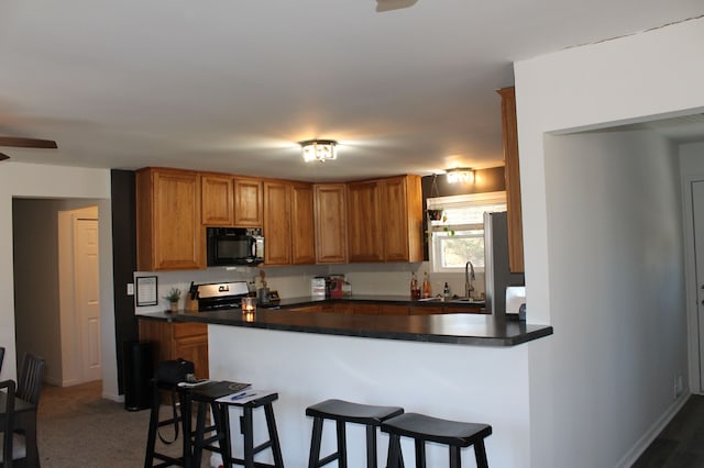 kitchen with dark countertops, a breakfast bar area, black microwave, and a sink